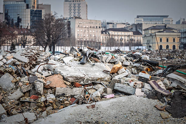 A close-up of construction debris and rubble from a demolished building site, showing broken concrete blocks, bricks, twisted metal rods, and other waste materials. Set against the urban skyline of Belgrade, Serbia, the image symbolizes urban renewal, construction activities, and the continuous transformation of modern cities.