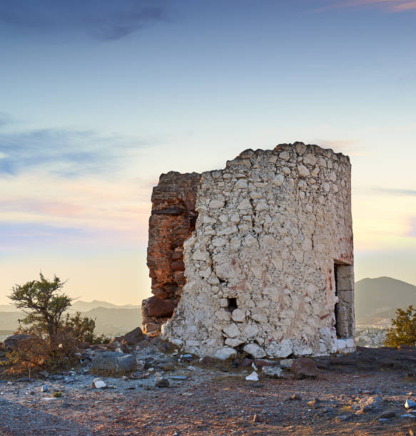 Historic stone windmills situated in Turkey amidst a serene mountainous background. The charming rustic architecture testifies to the region's cultural heritage, bathed in the golden hues of early morning sunlight. Close to the city of Bodrum.