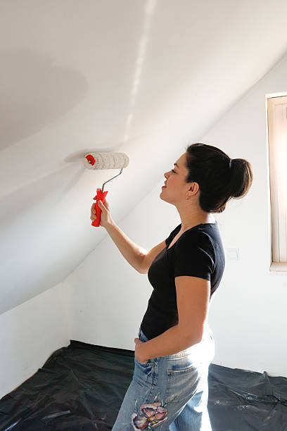 istock Renovation in progress - woman rolling white paint on the wall 2205795055