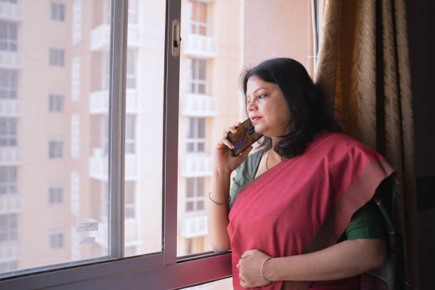 istock Indian Woman in Saree Talking on Mobile Phone by Window 2205798196