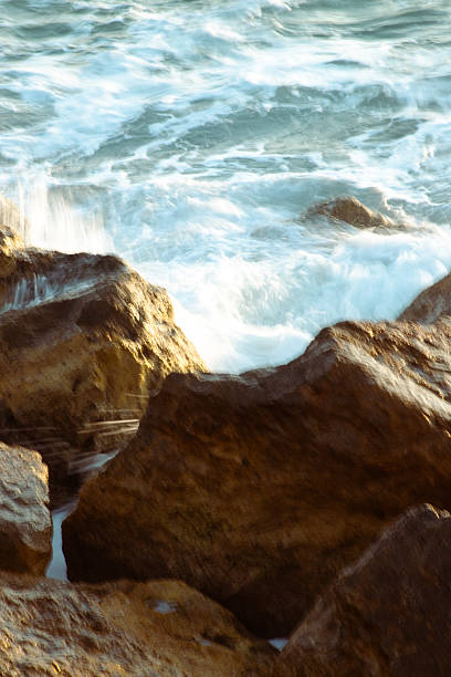 A close-up view of waves splashing against rocks, capturing the raw energy and movement of the sea. The image highlights the interplay between water and ston