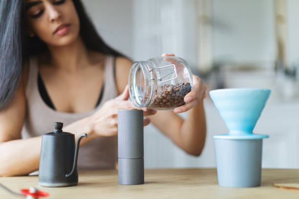 Young adult woman making coffee at home in the morning using coffee mill, grinder, brew coffee