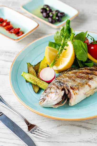 istock Grilled sea bream with vegetables and greens on white background 2205813399