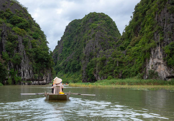 istock People on a boat floating down a river surrounded by tropical lush forests and mountains. Located in Tam Coc Ninh Binh Vietnam 2205814595