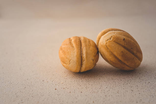 Stack of walnut-shaped cookies filled with caramel cream on light beige background. Homemade sweet dessert, traditional pastry, close-up of delicious treats. Cozy rustic style.