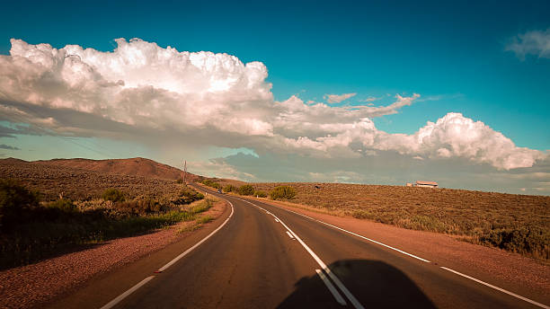 A long highway stretches into the Australian Outback, framed by dry bushland and distant hills, evoking adventure and freedom