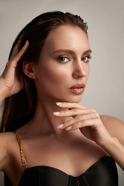 model with long hair strikes a confident pose in a stylish black outfit, using her hands to frame her face while exuding a sense of poise and charm within a well-lit studio