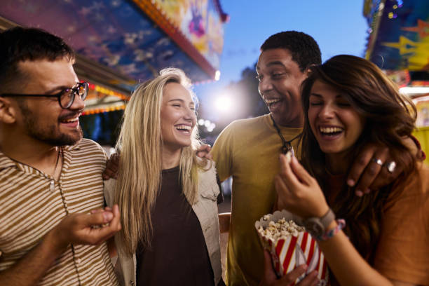 istock Happy couples talking while eating popcorn at amusement park. 2205820528