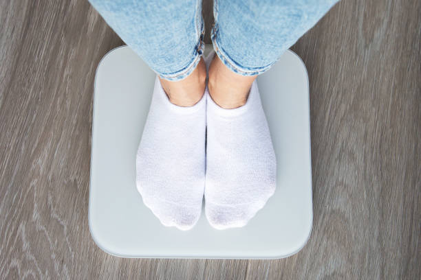 istock A person wearing white socks and jeans standing on a digital scale, viewed from above, symbolizing weight measurement and health monitoring 2205820841