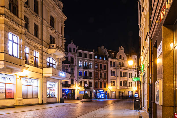 Torun, Poland - 03.14.2025: Shops glow softly as night envelops the old town of Torun, with Zegar clock tower standing proud amidst the tranquil streets.