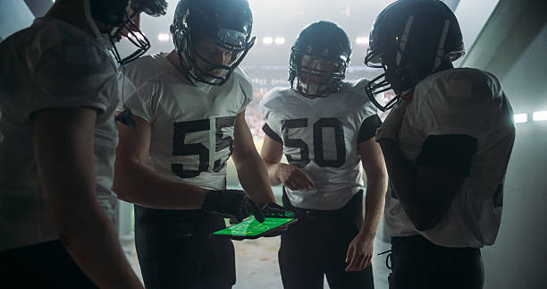 istock American Football Players Using Tablet Computer to Go Over Game Strategy Before Walking on Stadium Filled with Energetic Sports Fans and Team Supporters. Multiethnic Footballers Getting Ready 2205823433