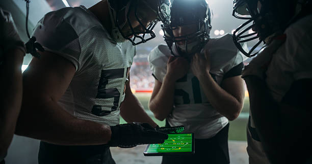 istock American Football Players Using Tablet Computer to Go Over Game Strategy Before Walking on a Stadium Filled with Energetic Sports Fans and Team Supporters. Multiethnic Footballers Getting Ready 2205823464