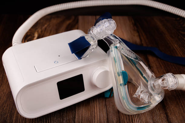 istock Sleep Apnea Therapy Equipment: White CPAP Machine with Display and Mask on Dark Table 2205823576