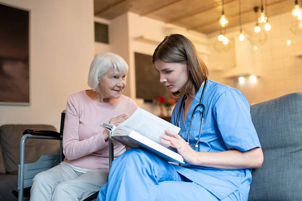 istock Female care assistant reading a book to a elderly lady and both looking enjoyed 2205824786