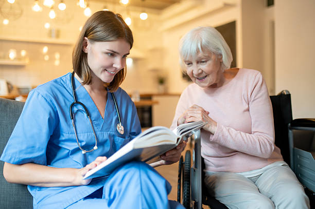 istock Female care assistant reading a book to a elderly lady and both looking enjoyed 2205824787