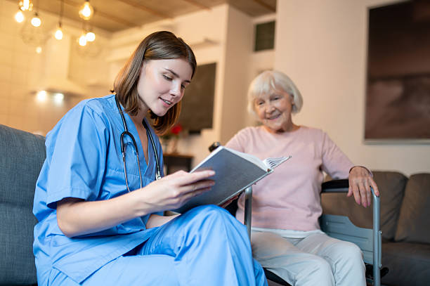 istock Female care assistant reading a book to a elderly lady and both looking enjoyed 2205824788