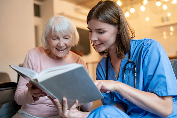 istock Female care assistant reading a book to a elderly lady and both looking enjoyed 2205824794