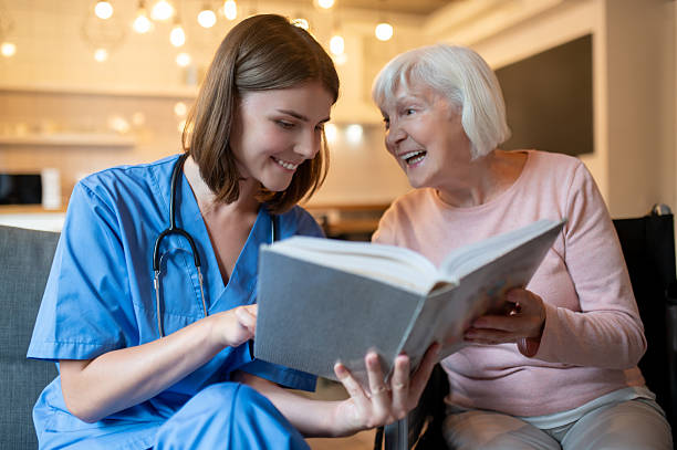 istock Female care assistant reading a book to a elderly lady and both looking enjoyed 2205824801