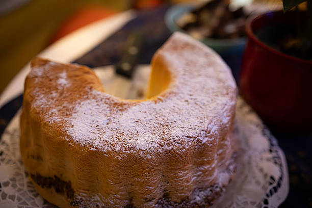 Delicious homemade Bundt cake dusted with powdered sugar, elegantly presented on a lace doily. The warm, festive background and classic baking style evoke a sense of holiday tradition and cozy seasonal gatherings. Perfect for use in winter recipe collections, holiday celebrations, and food-themed content.
