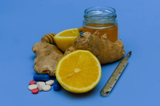A composition of natural remedies and pharmaceutical medications for treating cold and flu symptoms. The image features fresh lemon, ginger root, honey in a glass jar, a thermometer, and various pills on a blue background, symbolizing the contrast between traditional and modern medicine.
