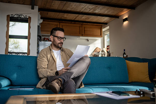 istock Focused man reading documents while sitting on a sofa in his living room 2205835675