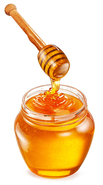 Honey dripping from honey spoon into honey pot on white background. File contains clipping path.