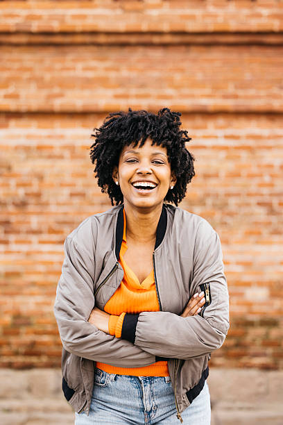 istock Young woman laughing with folded arms in front of brick wall 2205843527