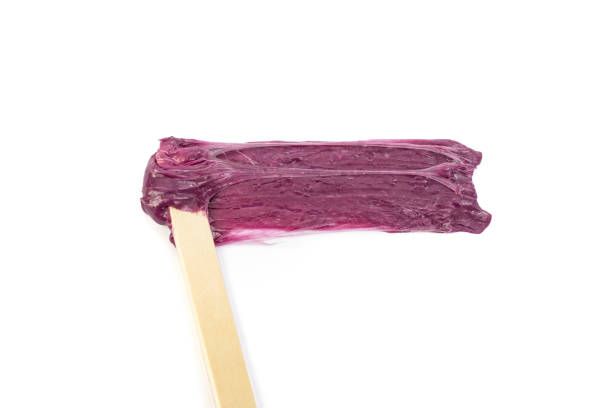 Professional skincare treatment shown with a gloved hand applying a clear gel or cream to the forearm using a wooden spatula. Clean, clinical, and focused on beauty and skin care.