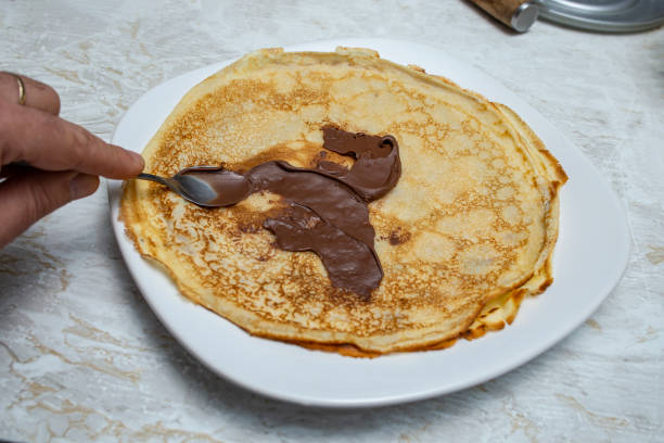 istock Spreading chocolate cream on a crepe pancake with a silver tea spoon 2205846495