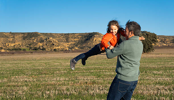 Father and daughter farmers smiling and looking at each other, leaning on a metal gate in their farm in australia