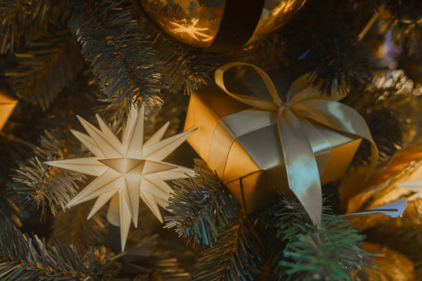 A golden box tied with a bow - a Christmas gift hangs in the branches of a Christmas tree.
