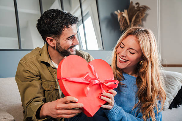 istock Couple Joyfully Celebrating Love with a Heart Shaped Gift Box, Exchanging Smiles and Affection, Perfect for Valentine's Day or Romantic Occasions, Capturing the Essence of Togetherness and Happiness 2205863718