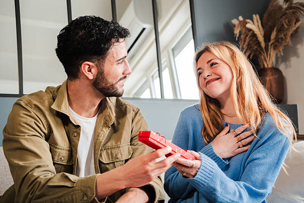 istock Joyful couple sharing a heartfelt moment while exchanging a surprise gift in a stylish and bright living space filled with natural light and elegant decor that enhances their intimate connection 2205865312