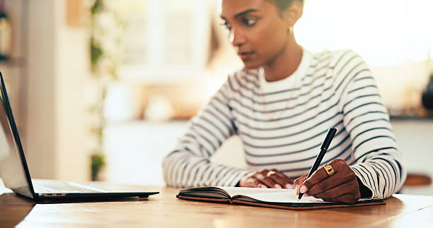 istock Education, writing and student with book, laptop or notes for online course in home, desk or college. Knowledge, reading and person with info for scholarship, university or learning for exam in house 2205872522