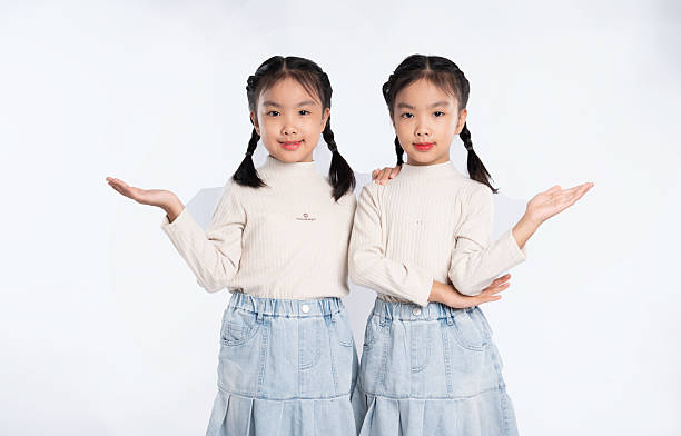 istock Two identical young sisters with braids presenting an offer with extended arms against a bright background. 2205873012