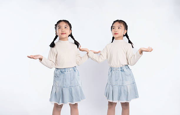 istock Identical twins present an unseen object with outstretched hands in studio, innocence and curiosity. 2205873215