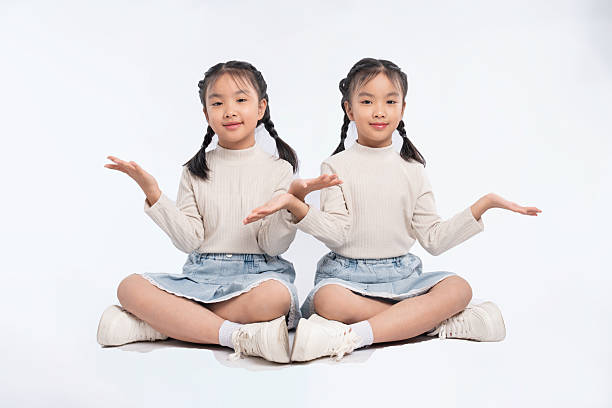 istock Identical twins present. Young girls with braids in matching outfits sit in a studio with open palms. 2205873456
