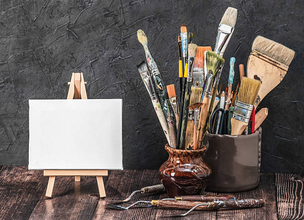 istock Creative composition with miniature canvas on an easel and vintage paint brushes on a wooden table. Artistic creativity concept. 2205874760