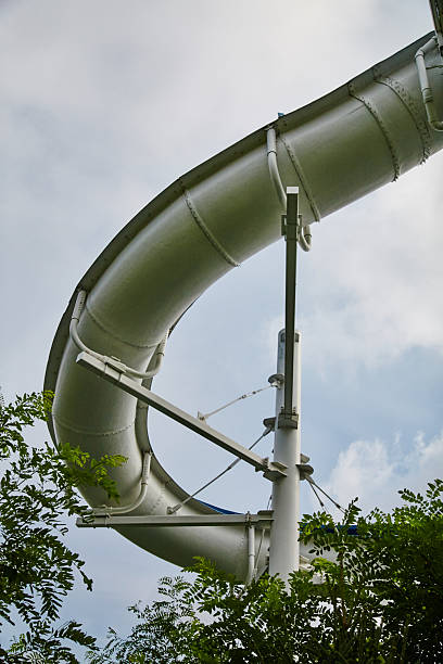 Curved Giant Water Slide with Green Foliage - Ground Up View Large Silver-Grey Water Slide Towering Above Green Foliage in Abandoned Fun Spot Amusement Park, Angola, Indiana, 2015 top of water slide photos stock pictures, royalty-free photos & images