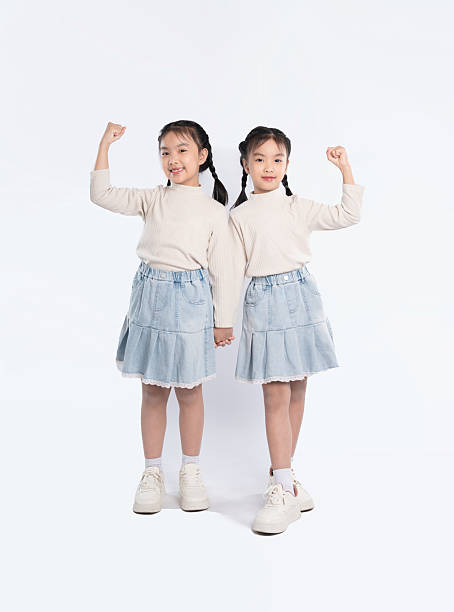 istock Twin sisters in matching outfits, showcasing strength and unity against a white background, holding hands. 2205876722