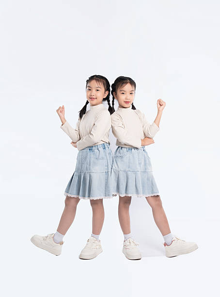 istock Twins posing back to back in matching outfits with confidence against a plain white background. 2205876747