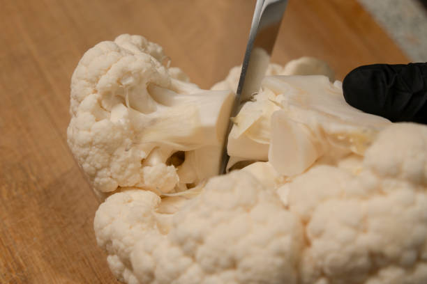 istock Chef cuts a head of cauliflower into florets on a kitchen cutting board. Close-up 2205877966