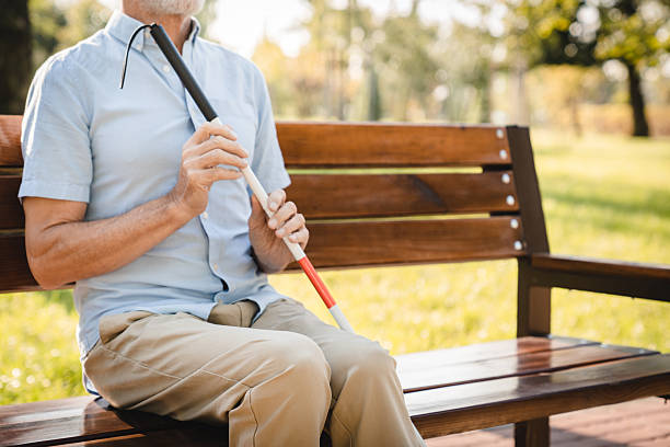 istock A visually impaired blind senior man in casual outfit holding using a white and red guide cane walking stick, sitting outdoors on a wooden bench in park. Vision problems concept copy space 2205882575