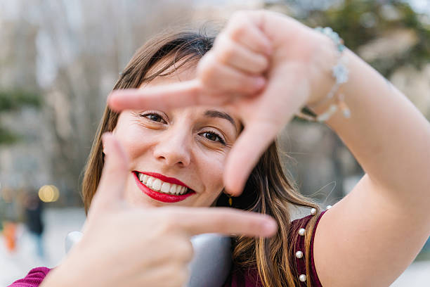 istock Young woman framing her face with hands, smiling brightly at the camera while enjoying a sunny day in the vibrant city streets 2205883356