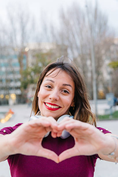 istock Smiling woman creating a heart shape with her hands while enjoying the outdoors, radiating happiness and affection in an urban setting 2205883382