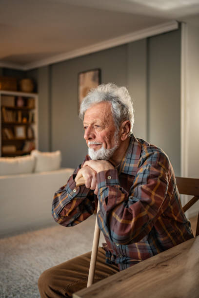 istock Senior man sitting at home with walking cane, looking away thoughtfully 2205884413