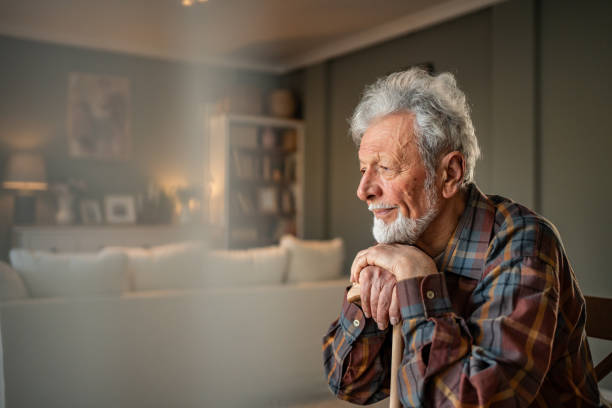 istock Senior man sitting at home with walking stick, looking out window 2205884482