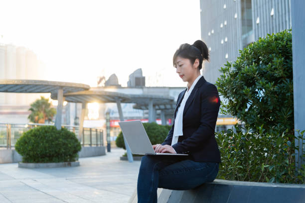 istock Businesswoman using laptop outside the office building 2205895416