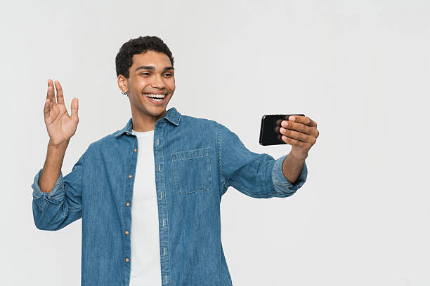 istock Smiling Young Man Waving While Taking a Selfie on a Smartphone 2205895641