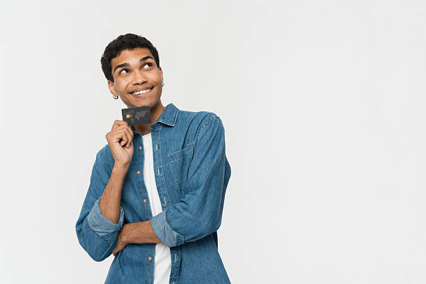 Smiling Young Man Holding a Credit Card in a Thoughtful Pose